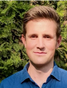 A student with short light brown hair wearing a blue dress shirt